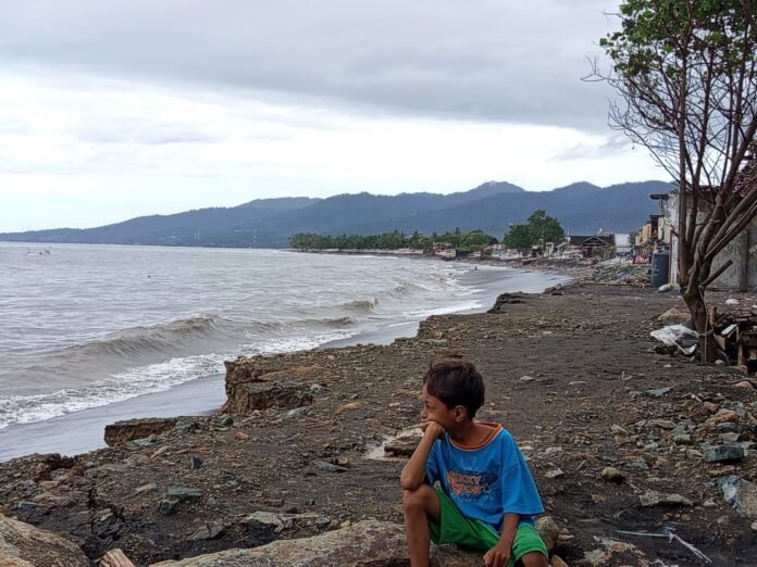 DUDUK - Seorang anak duduk di pinggir pantai di Lingkungan Bugis, Kelurahan Bintaro, Kecamatan Ampenan pada Minggu, (12/7/2026). Pembangunan tanggul pemecah gelombang ditargetkan 2027, diprioritaskan di Bintaro. (Suara NTB/pan)
